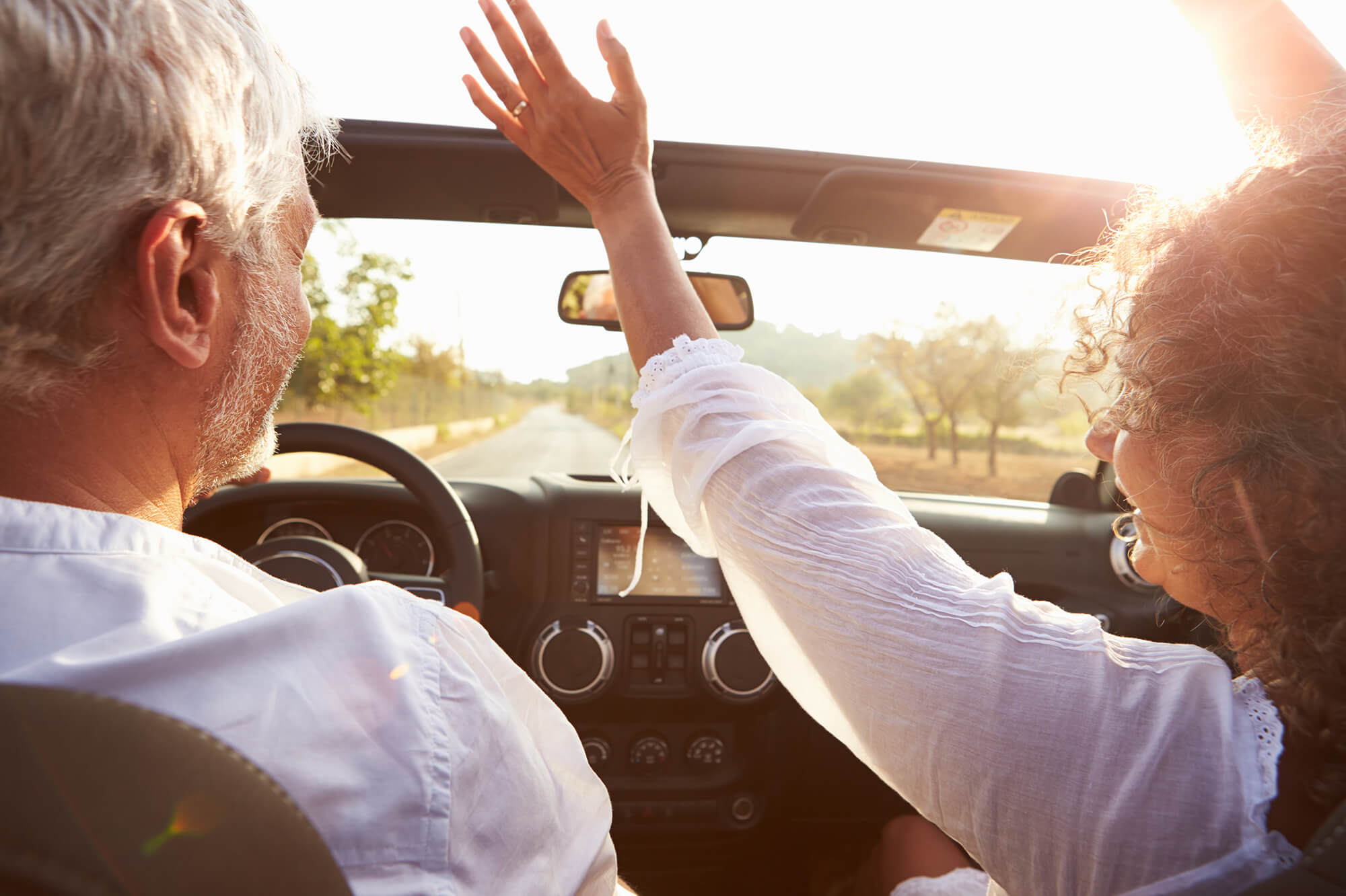 Couple driving along country road in open top car